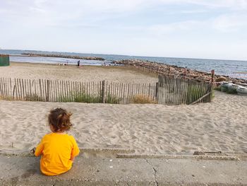 Rear view of girl sitting at beach against sky