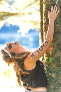 Smiling woman embracing tree trunk in forest