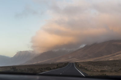 Road by mountains against sky during sunset