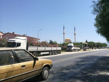 Cars on road by buildings against clear blue sky