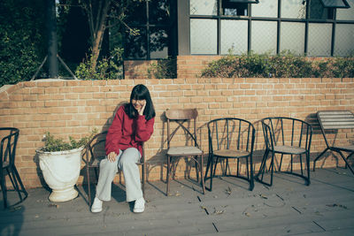 Asian teenager wearing red sweater sitting on wood desk