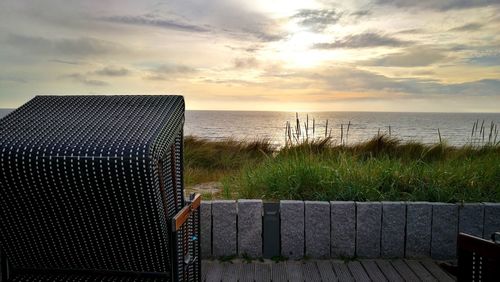 Hooded chairs on beach against sky during sunset