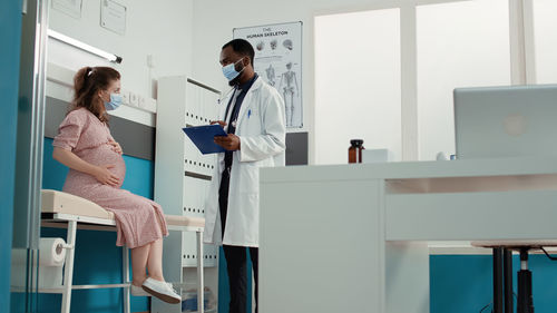 Doctor holding file folder taking with pregnant woman at clinic