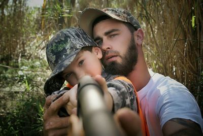 Close-up portrait of son with father holding gun