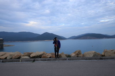 Rear view of man standing on lake against mountains