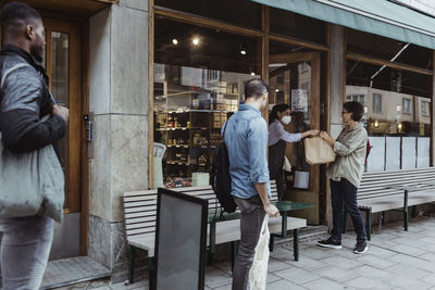 Female customer collecting package food from sales woman at deli store during covid-19