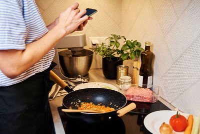 Woman cooking sauce bolognese and use smartphone