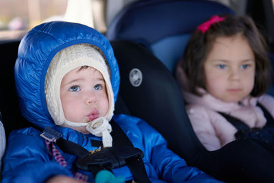 Siblings sitting in safety chairs in the back seat of a car