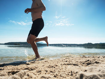 Muscular shirtless man is running in water at the beach.