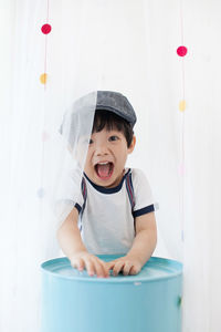 Portrait of cheerful boy screaming while standing by curtains at home
