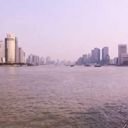 Sea by cityscape against sky during sunset