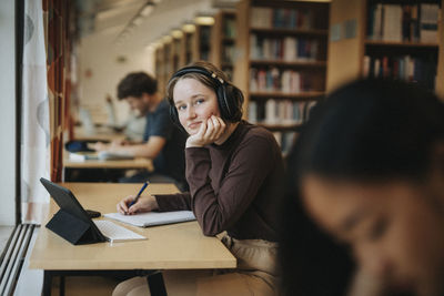 Portrait of smiling student wearing headphones while studying in library at university