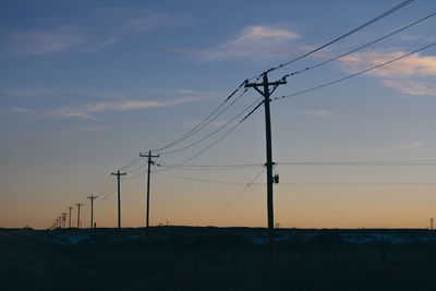 Low angle view of electricity pylons against sky during sunset
