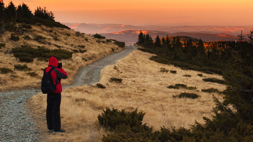 Rear view of woman standing on land against sky during sunset