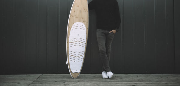 Low section of man with surfboard standing against wall