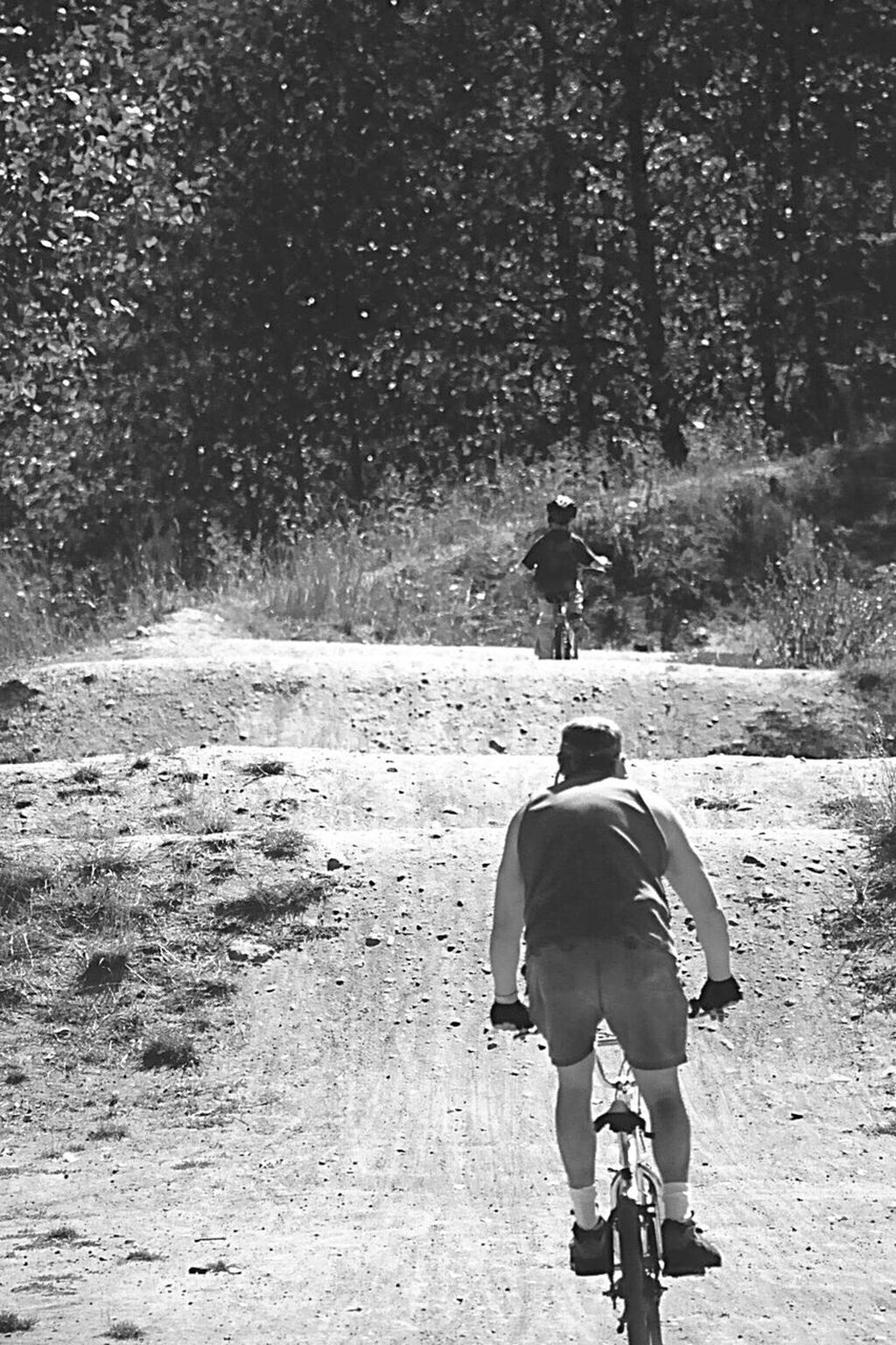 Dad & Son Racing Bikes. Dad Letting Son Win. BMX Track, Fir Tree Landscape, Dusty Trail,
