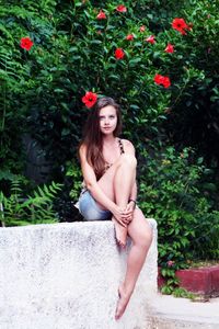 Portrait of young woman sitting on railing against plants