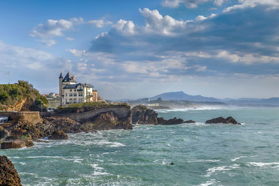 Buildings by sea against cloudy sky