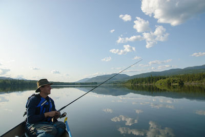 Man fishing in lake against sky