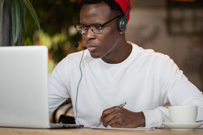 Young man writing on paper while looking at laptop