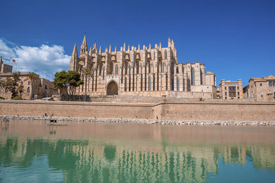 Medieval la seu cathedral reflecting in canal water against blue sky at city