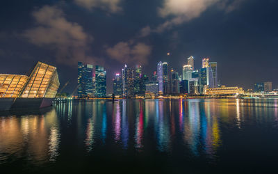 Illuminated buildings by river against sky