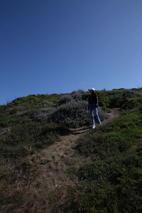 Rear view of man walking on field against clear sky