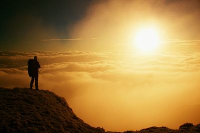 Silhouette man standing on rock against sky during sunset