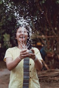 Young woman splashing water while holding bowl outdoors