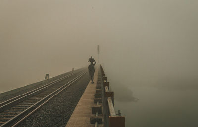 Rear view of man walking on railway bridge amidst fog