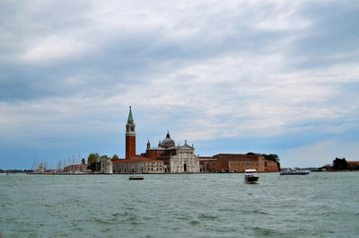 View of buildings by sea against cloudy sky