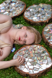 Top view portrait of a young woman lying on a lawn among stumps covered with a mirror