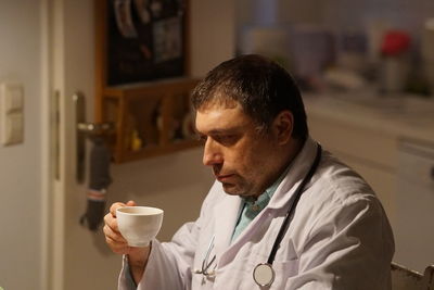 Side view of thoughtful mature doctor with coffee sitting in hospital