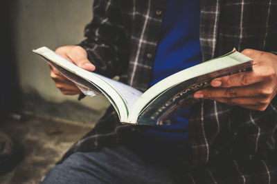 Midsection of man holding book while sitting outdoors