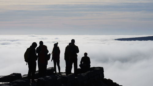 Silhouette people standing on rock against sky