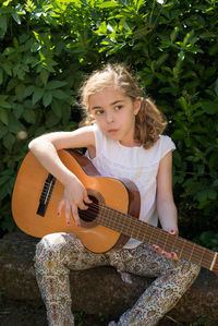 Girl playing guitar while sitting on rock against plants