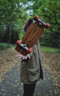 Person balancing skateboard while standing in forest