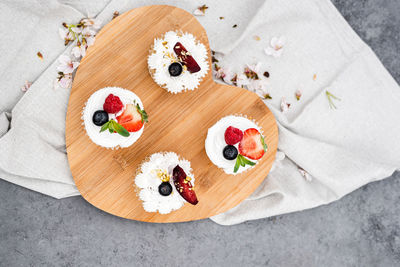 Top view of vegan cupcakes with berries and coconut cream on a wooden board.