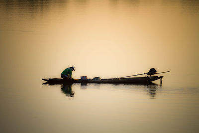 Silhouette man in boat on lake against sky during sunset