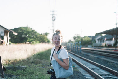 Portrait of cheerful woman standing by railroad track