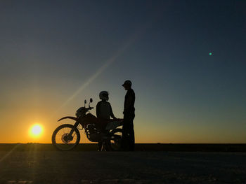 Friends talking while standing by motorcycle on land against sky during sunset