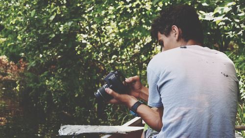 Rear view of man using camera against trees in forest