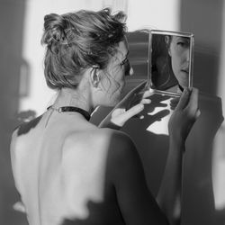 Shirtless woman looking in mirror against wall
