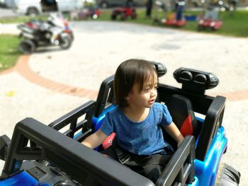 Baby girl sitting in toy car on footpath at park