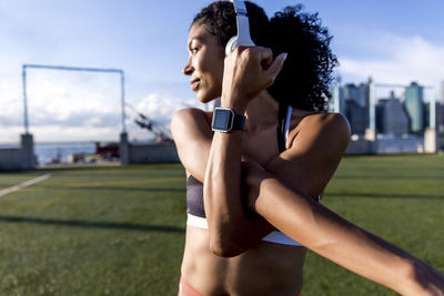 Athlete stretching hands while standing on grassy field during sunny day against sky