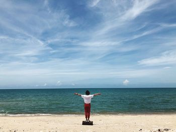 Rear view of woman with arms outstretched while standing on beach against sky