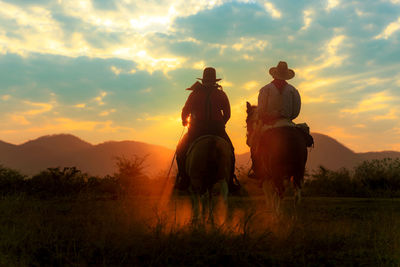 Men riding horse on field against sky during sunset