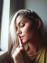 Close-up portrait of woman with finger on lips by window at home