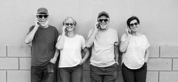 Portrait of senior people using mobile phones while standing against wall 