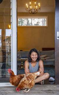 Woman sitting in the doorway of house and feeding the domestic birds